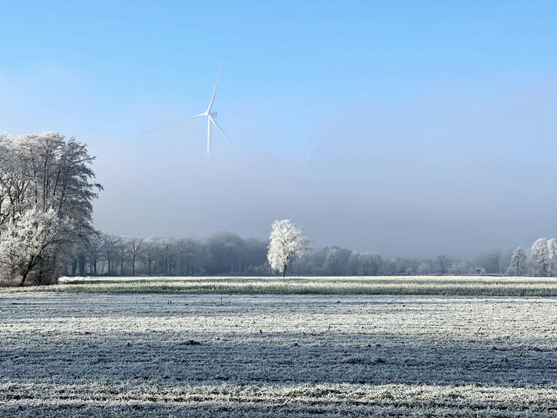 A winter landscape with a wind turbine half covered in mist